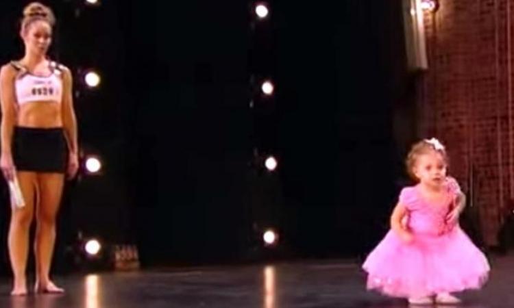 À 2 ans, elle suit sa maman sur scène dans sa petite robe rose. Gardez bien les yeux sur ses pieds!